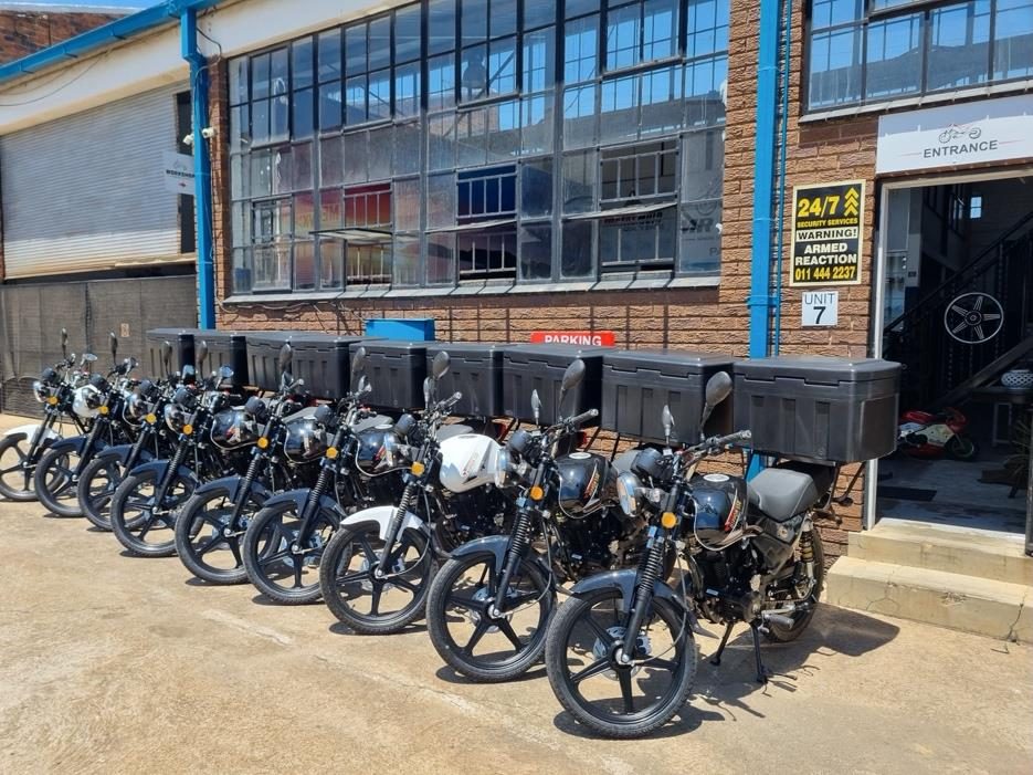 A fleet of delivery-ready Nippon 150 motorcycles with rear boxes outside Mr Bikes